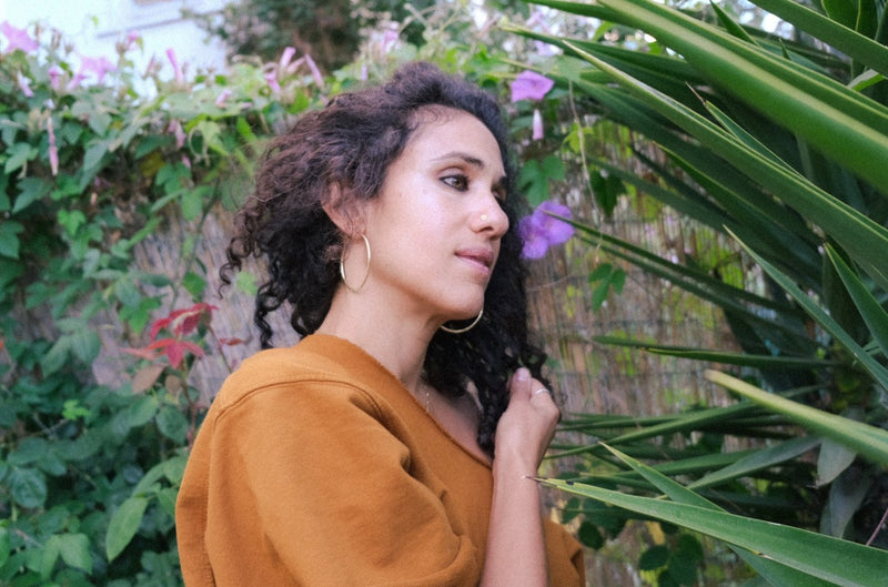 naima wearing 2 inch brass hoops in garden with green plants around her